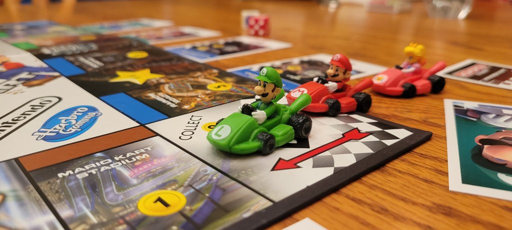 A close up of Monopoly Gamer: Mario Kart. Mario, Luigi, and Princess Peach are all driving go-karts into the "GO!" space, approaching Mario Circuit.