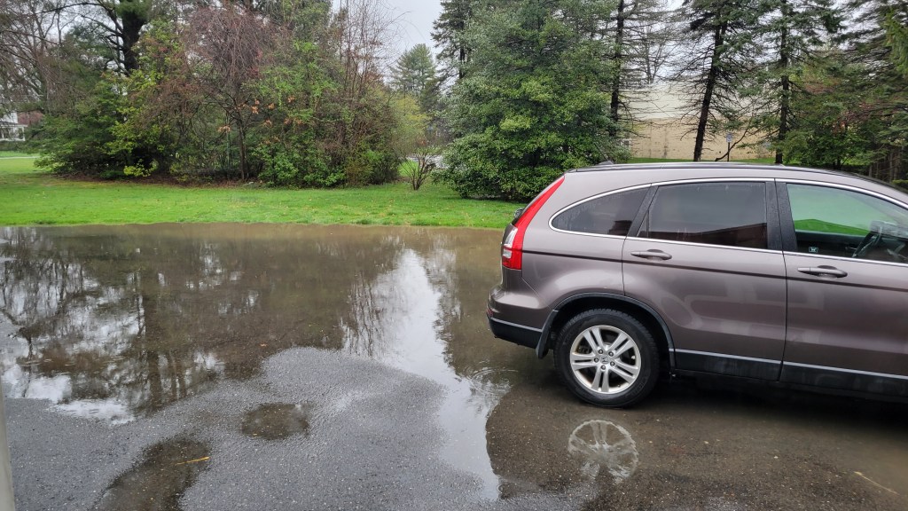 A silver SUV parked in a driveway flooded with about an inch of water.